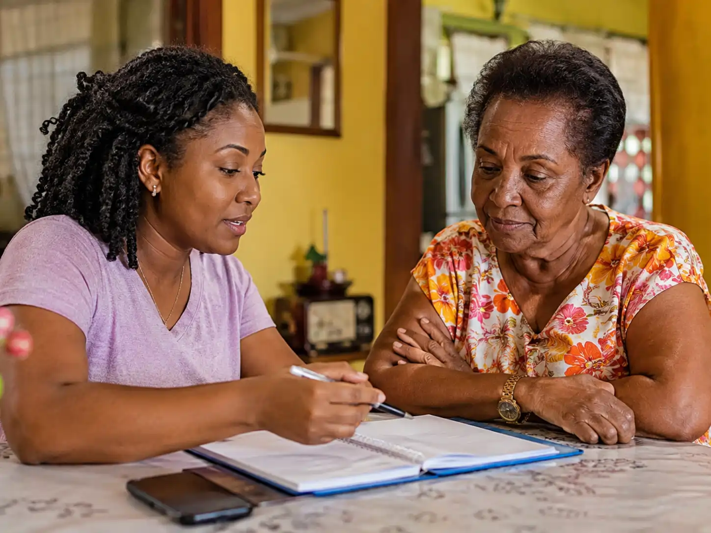Older Jamaican parent and family-support coordinator reviewing a simple local support plan at a table